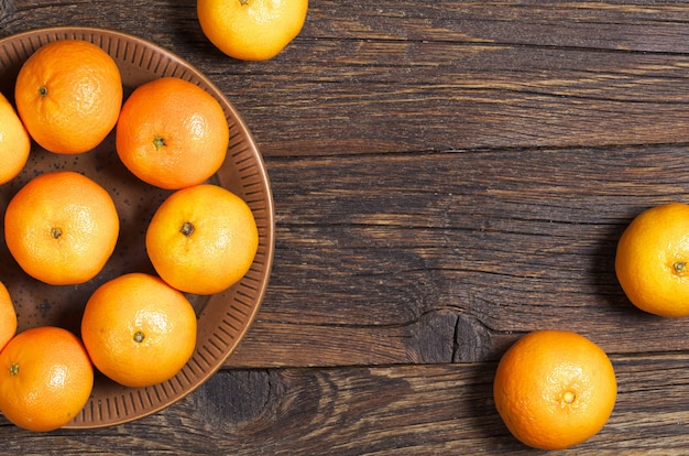 Mandarinas en placa y cerca de la mesa de madera oscura, vista superior