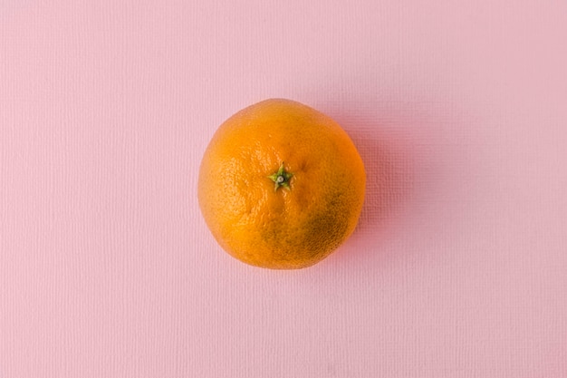 Foto mandarine auf rosa-pastellfarbenem hintergrund. die mandarine liegt in der mitte.