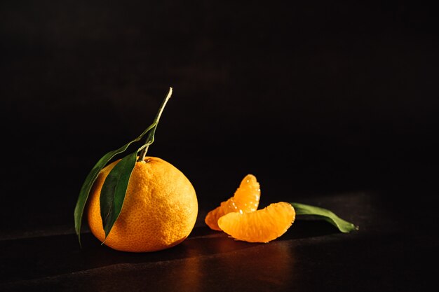 Mandarine mit Blättern und Scheiben auf einer schwarzen Oberfläche