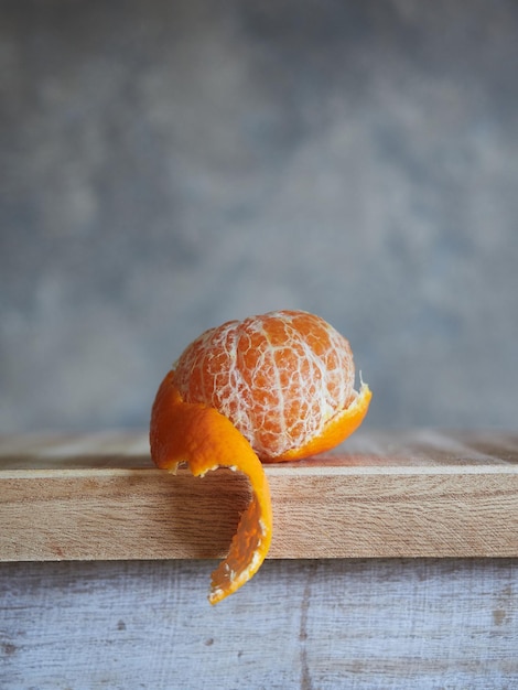 Mandarine mit teilweise abgezogener Haut auf Holz und grauem strukturiertem Hintergrund