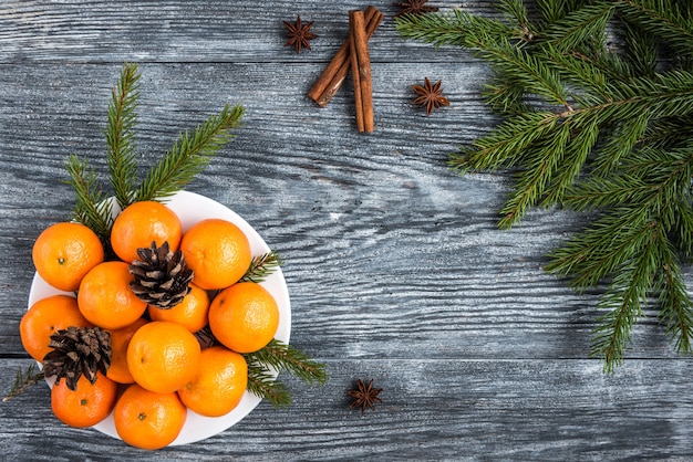 Mandarinen auf Holz mit Weihnachtstannenzweigen, Zimtstangen, Anissternen und Zapfen.