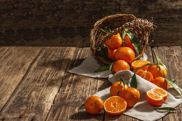 Mandarinen fallen aus dem Korb. Orangen, Mandarinen, Clementinen, Zitrusfrüchte) mit grünen Blättern. Hölzerner Hintergrund, rustikaler Stil, Kopienraum