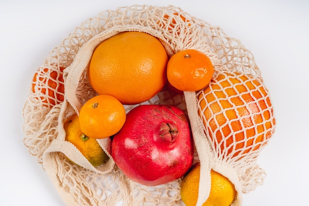 Mandarinen, Grapefruit und Granatapfelfrüchte liegen in einem Baumwoll-Ökobeutel auf weißem Hintergrund