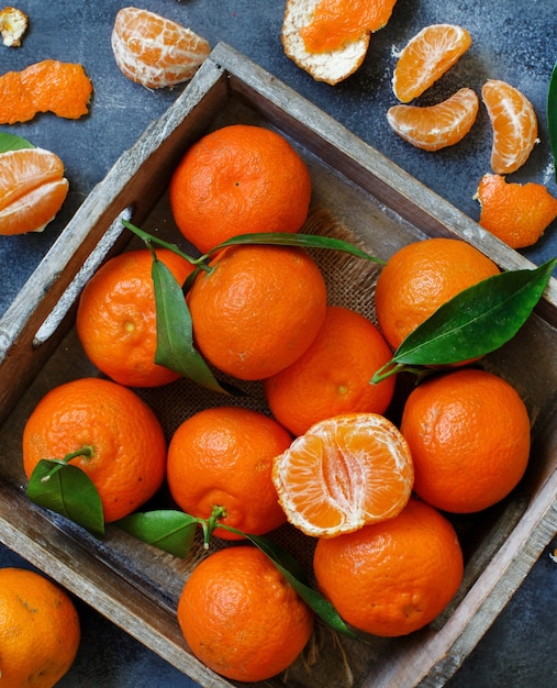 Mandarinen mit Blättern in einer Box auf grauem Hintergrund