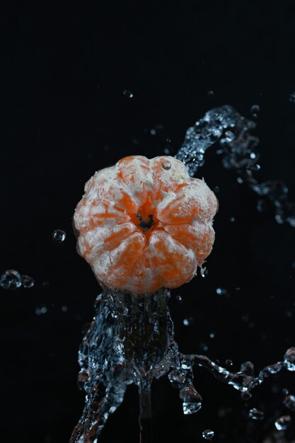 Mandarinen mit Spritzwasser auf schwarzem Hintergrund.