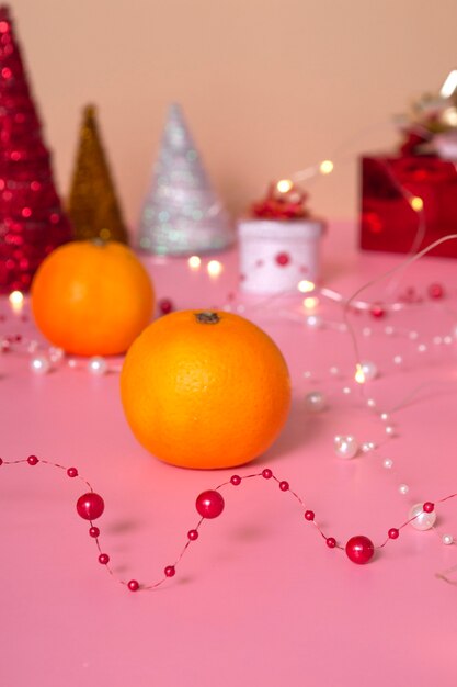 Mandarinen Nahaufnahme und im Hintergrund ein fabelhaftes rotes Geschenk mit einem goldenen Band und einem Weihnachtsbaum auf rosa Hintergrund. Silvester und Weihnachten. Platz kopieren. Vertikal