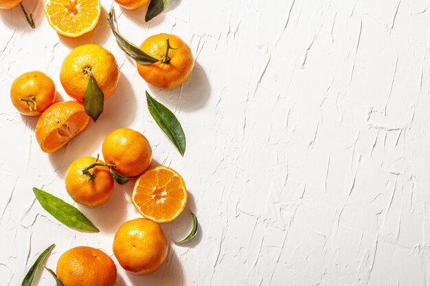 Mandarinen (Orangen, Mandarinen, Clementinen, Zitrusfrüchte) mit grünen Blättern. Modernes hartes Licht, dunkler Schatten. Weißer Kitthintergrund, kreative flache Lage, Draufsicht