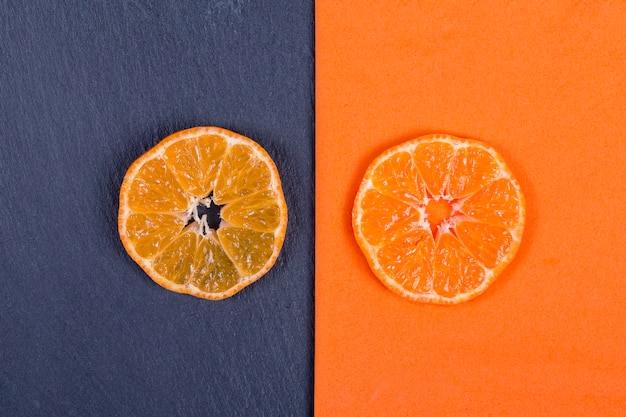Mandarinenscheiben liegen auf orangefarbener Serviette und auf schwarzem Schiefer