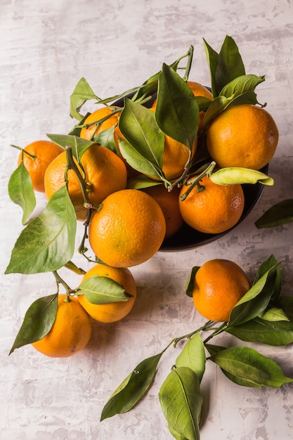 Los mandarines o las mandarinas maduros anaranjados dan fruto con las hojas verdes, sobre fondo de madera rústico.