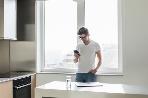 Mandava um jovem bonito com seu smartphone na cozinha