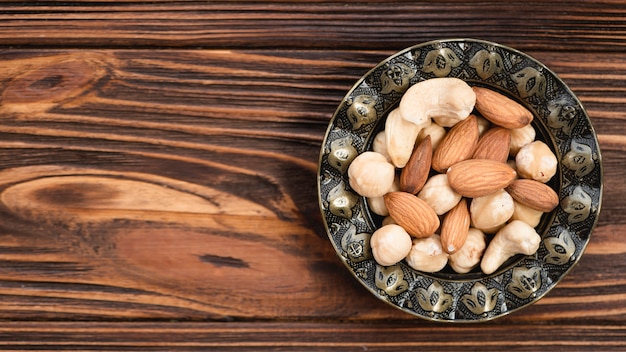 Mandel; Cashewnuss und Haselnüsse in der antiken metallischen Schüssel auf hölzernem Schreibtisch