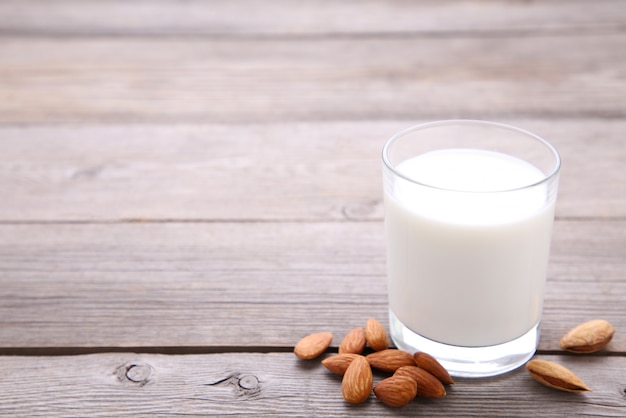 Mandelmilch im Glas mit Mandeln auf grauem hölzernem