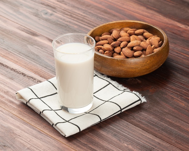 Mandelmilch im Glas mit Mandeln in Holzschale auf dem Tisch, gesunder Snack, vegetarisches Essen.