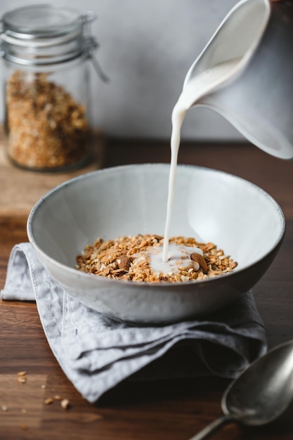 Mandelmilch wird in eine Keramikschale mit gebackenem Müsli gegossen. Gesundes vegetarisches Frühstück