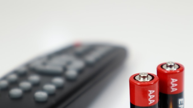 Mando a distancia del televisor negro con pilas alcalinas AAA en rojo y blanco sobre fondo blanco. Reemplazo de batería, repuestos. Primer plano del compartimento de la batería del mando a distancia.