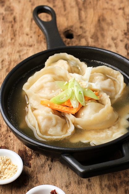 Mandu Guk, sopa de bola de masa coreana con aderezo de cebolleta y huevo frito en rodajas, servida con hojuelas de chile y semillas de sésamo