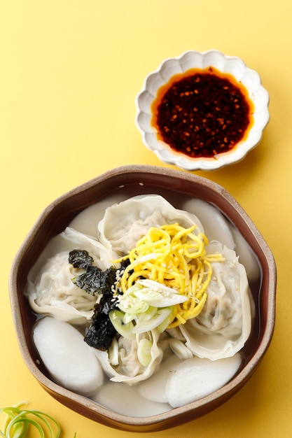 Mandu Tteokguk Suppe oder Reiskuchen in Scheiben und Knödelsuppe Seollal Festival Food Draufsicht auf gelbem Hintergrund