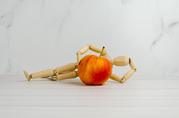 Manequim de madeira encontra-se em pose relaxada contra o fundo da maçã. conceito de pensar sobre uma ideia