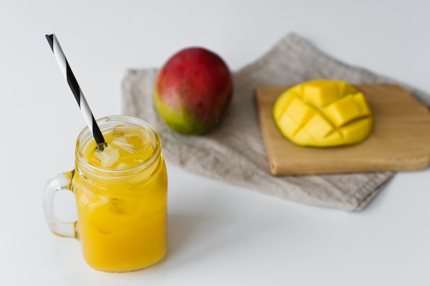 Manga madura, meia manga e um copo de suco de manga em uma tábua de madeira.