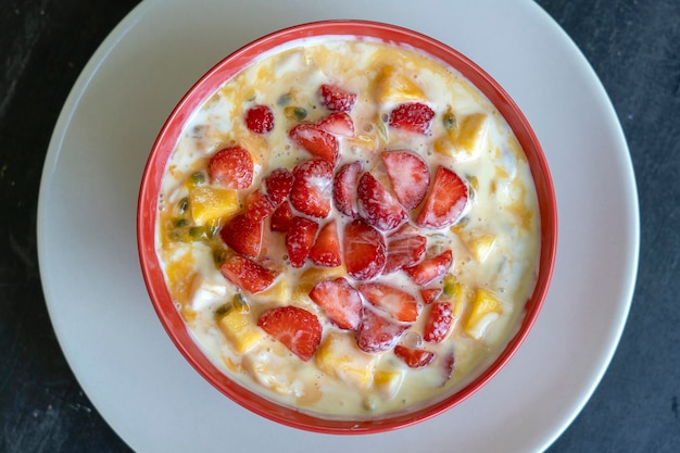 Manga, maracujá, morango vermelho e iogurte brulee. Sobremesa de frutas no café da manhã com fatias de manga e morango perfeitamente maduras na estação, polpa de maracujá fresca coberta, close up