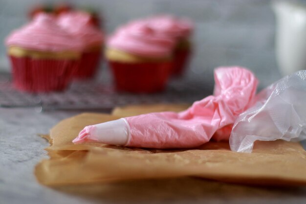 Manga pastelera y muffins de vainilla con glaseado de crema de mantequilla de fresa rosa encima, mesa de mármol gris