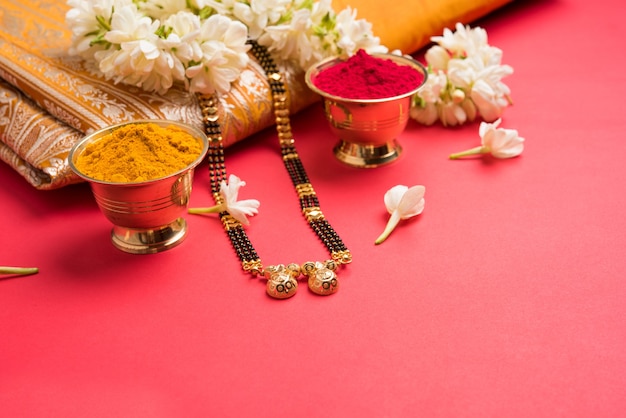 Mangalsutra oder goldene Halskette, die von verheirateten hinduistischen Frauen getragen wird, arrangiert mit traditionellem Saree mit Huldi Kumkum und Mogra-Blumen-Gajra, selektiver Fokus