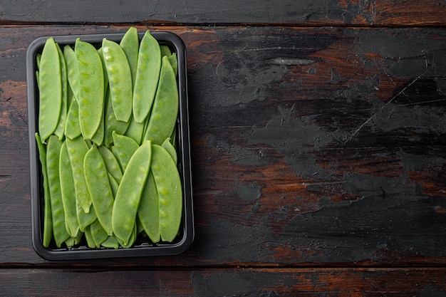 Mangetout orgânico fresco, também conhecido como conjunto de ervilha-de-açúcar, em um recipiente de plástico, na velha mesa de madeira escura