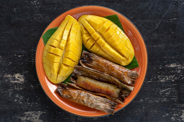 Mango amarillo de postre de estilo tailandés con arroz pegajoso de plátano en hojas de palma Mango amarillo y arroz pegajoso es comida tradicional popular de Tailandia Primer plano