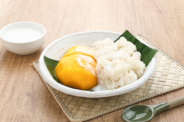 Mango con arroz pegajoso, postre tailandés. Servido en plato blanco sobre fondo de madera