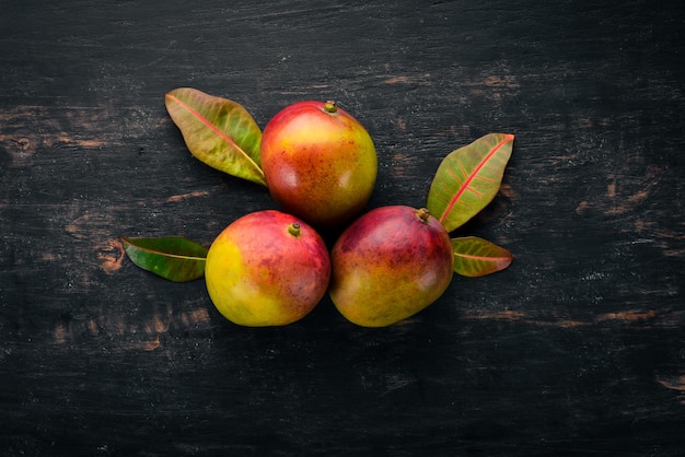 Mango con hojas sobre un fondo de madera negra Frutas tropicales Vista superior espacio libre para su texto