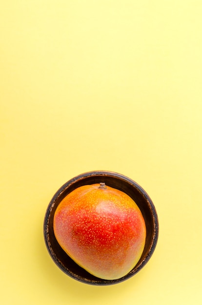 Mango jugoso fresco en una placa de arcilla marrón sobre un uniforme amarillo