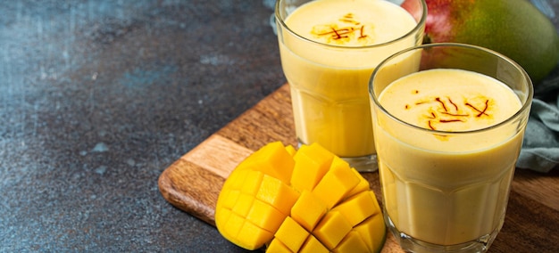 Mango-Lassi in zwei Gläsern auf rustikalem Betontisch mit frisch geschnittenem Manfo von oben trinken