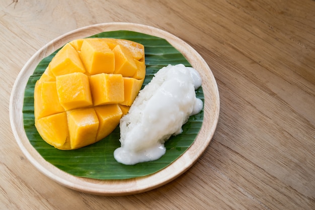 Mango maduro con arroz pegajoso y leche de coco, postre tailandés en hoja de plátano, textura de madera