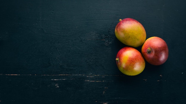 Mango mit Blättern auf schwarzem Holzhintergrund Tropische Früchte Draufsicht freier Speicherplatz für Ihren Text