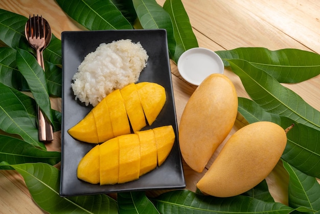 Mango mit klebrigem Reis auf schwarzem Teller Gelbe Mango mit klebriger und Kokosmilch ein thailändisches Dessert