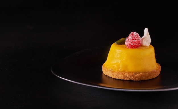 Foto mango-mousse-kuchen-dessert bedeckt mit gelber glasur auf schwarzem teller