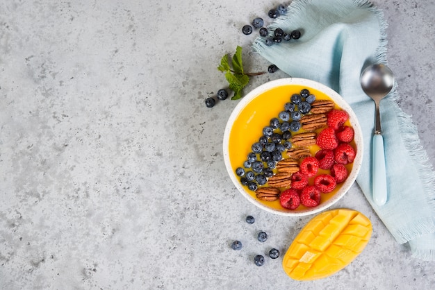 Mango-Orangen-Smoothie-Schüssel mit frischen Beeren und Nüssen.