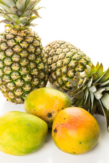 Mango y piña orgánicos frescos en una tabla de madera blanca.