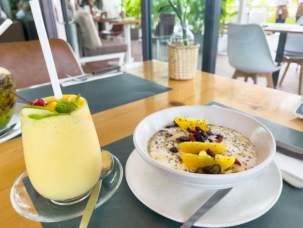 Foto mango-smoothie und joghurt-müslischale mit früchten auf dem café-tisch. gesundes boost-frühstückskonzept