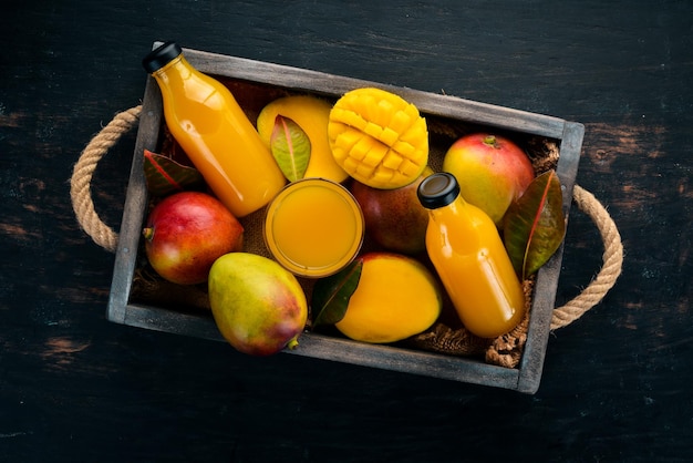 Mango und Saft in einer Holzkiste Auf einem hölzernen Hintergrund Tropische Früchte Draufsicht Kostenloser Kopierbereich