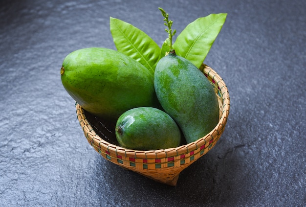 Mango verde, fruta de verano y hojas verdes en la canasta en la oscuridad.