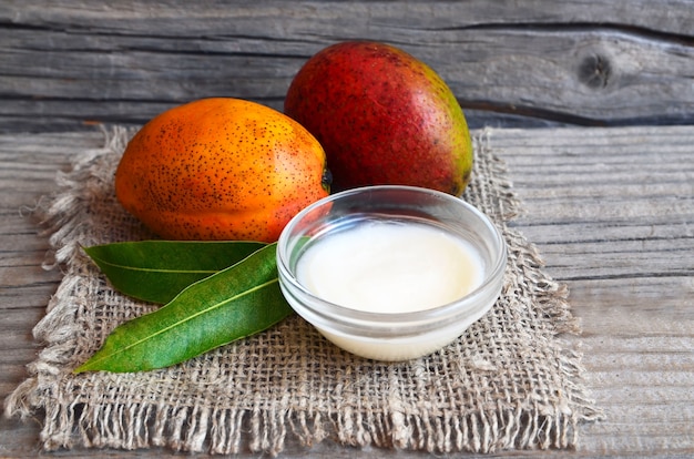 Mangokörperbutter in einer Glasschüssel und in frischen reifen organischen Mangofrüchten auf altem Holz