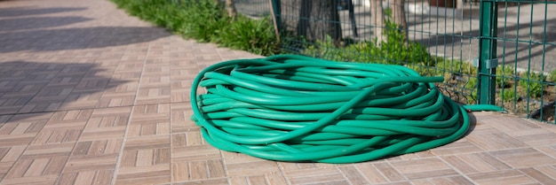 Manguera de goma verde retorcida para regar las plantas en la acera