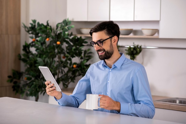 Manhã agradável Empresário bonito e alegre bebendo chá enquanto estiver usando o tablet