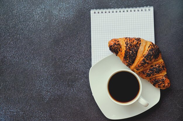 manhã. café da imprensa francesa, xícara de café quente e croissant doce em fundo preto. Vista do topo