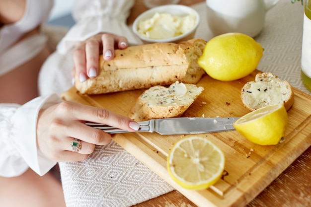 Manhã Café da manhã pão com manteiga, limonada e limões. Uma mulher espalha manteiga no pão