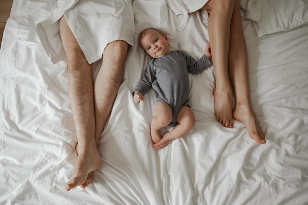 Manhã de jovem casal feliz em roupões de banho brancos com o bebê na cama em casa.