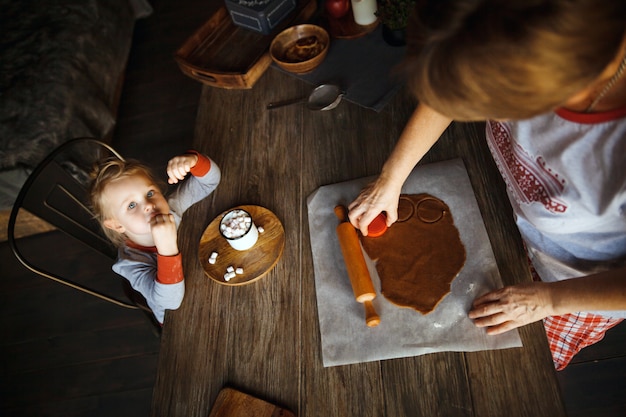 Manha de natal. vovó cozinhava biscoitos de gengibre e neta bebendo chocolate com marshmallows.