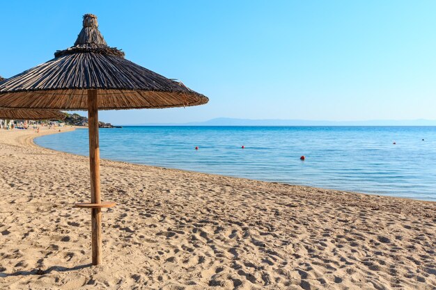 Manhã de verão na praia de Platanitsi com guarda-sol de palha (Halkidikii, Grécia). Povos irreconhecíveis.