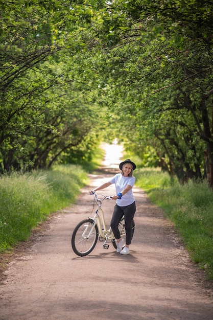 Manhã de verão. Uma mulher com uma bicicleta em uma estrada no parque